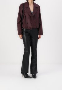Bordeaux cropped jakke med en dobbelbrystet design og sorte knapper, parret med tætsiddende sorte imiteret læderbukser og spidse ankelstøvler.