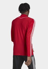 Rotes Langarm-Trikot mit Mesh-Struktur, das weiße vertikale Streifen entlang der Ärmel und ein kontrastierendes weißes Halsbündchen aufweist.