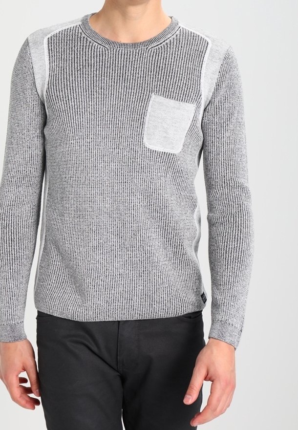 Pull en maille gris avec motif côtelé texturé, épaules contrastantes en gris clair et poche poitrine. Porté avec un pantalon noir.