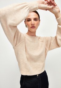 Heller rosa Pullover mit Ballonärmeln und gerippten Bündchen. Weicher Stoff, runder Ausschnitt, kombiniert mit dunklen Jeans. Elegante Silhouette.