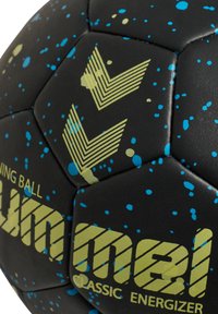 Czarna piłka treningowa z heksagonalnymi panelami, z niebieskimi i żółtymi rozproszonymi wzorami oraz diagonalnym logo. Tekst: "Klasyczny Energetyk."