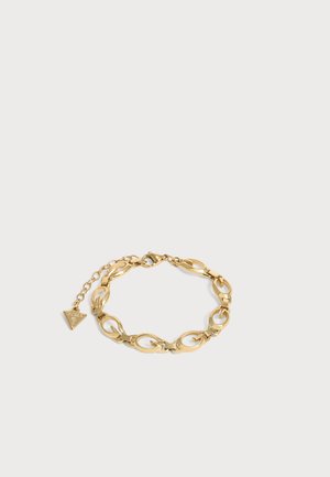 Bracelet en métal doré avec des maillons ovales et un petit pendentif triangulaire gravé du nom de la marque, relié à une chaîne ajustable.