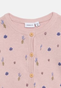 Ροζ πλεκτό μπουφάν μωρού με μικρά μπλε και μωβ λουλουδάτα σχέδια και τρία ανοιχτόκαφέ κουμπιά μπροστά.