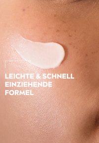 White cream swatch on smooth, light brown skin, showcasing a slightly glossy texture. Text on the left reads: "Leichte & schnell einziehende Formel."