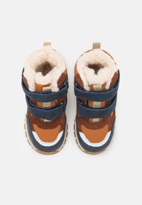 Brązowe i granatowe buciki dla malucha z dwoma paskami na rzep, miękką kremową wyściółką, zaokrąglonym noskiem oraz teksturowaną podeszwą zapewniającą przyczepność.