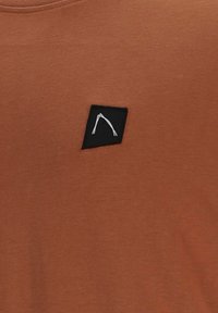 Tessuto di colore ruggine con una piccola toppa nera al centro, con un semplice motivo astratto a linee bianche.