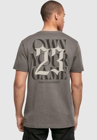 Grå bomulds t-shirt med fedt grafisk tekst på ryggen: "TAG ANSVAR FORDIT" og "GØR DET LEGENDARISK" med et stort "23" i creme.