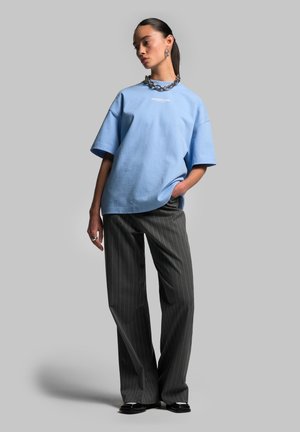 Light blue oversized T-shirt with short sleeves and a crew neckline, paired with charcoal pinstripe wide-leg pants. Silver chain necklace.