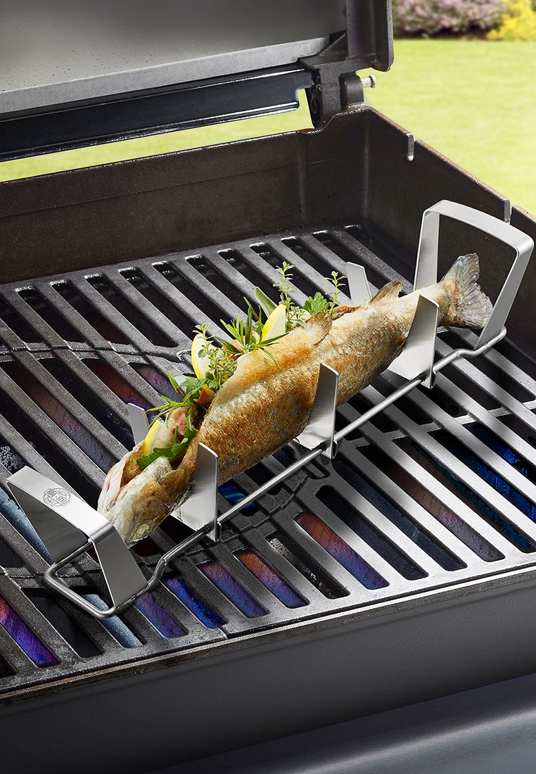 Stalowa ruszty do grillowania, na którym znajduje się cała ryba, udekorowana ziołami i cytryną, na grillu gazowym z widocznymi elementami grzewczymi.
