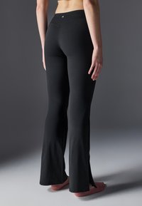 Pantaloni de yoga negri, evazați, fabricați dintr-un material moale și elastic, cu o talie înaltă. Au fante laterale la tiv pentru o ventilație suplimentară.