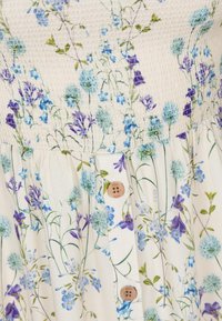 Bloemenjurk met een smock-bustier, lichtgewicht crèmekleurige stof, lichtblauwe en paarse bloemen, en houten knopen aan de voorkant.