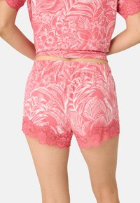 Rosa blommiga shorts i mjukt tyg, med vita botaniska mönster och en scalloped spetskant. Elastisk midja för komfort.