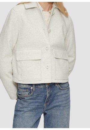 Veste en laine gris clair avec grandes poches avant à rabat et boutons, portée sur un pull crème et un jean bleu.