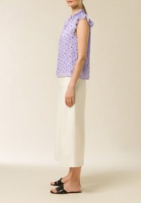 Blusa lilla con maniche a balza, caratterizzata da un motivo a righe verticali e piccoli cuori blu. Abbinata a pantaloni larghi crema e sandali neri.