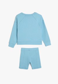 Sudadera de manga larga azul claro con textura acanalada, combinada con pantalones cortos a juego. Ambos presentan costuras visibles y un ajuste relajado.
