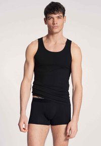 Zwarte geribbelde tanktop gecombineerd met bijpassende zwarte boxershorts, met een nauwe pasvorm en een zachte textuur, getoond op een mannelijke model.