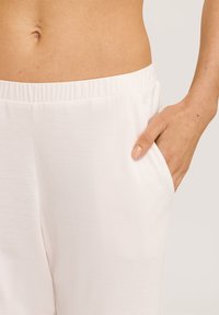 Lichtroze, gestructureerde stof sweatpants met een elastische tailleband en zijvakken. Een hand rust in de zak, zodat de pasvorm wordt getoond.