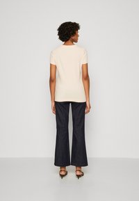 Camiseta ajustada de color beige claro, con mangas cortas, combinada con jeans de pierna ancha de color azul oscuro. Textura suave, diseño minimalista, escote redondo sencillo.