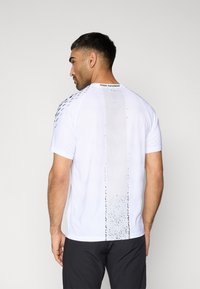 Λευκό αθλητικό κοντομάνικο πουκάμισο με υφασμένο σχέδιο, λογότυπο Venum Performance στη ράχη και κυματιστό κάθετο σχεδιαστικό στοιχείο.