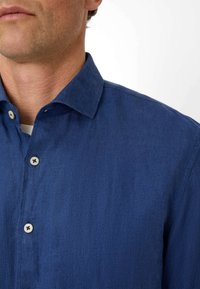 Blue button-up shirt with a collar, crafted from a textured fabric. Features light buttons with dark holes and a neat fit.