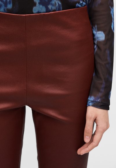 Burgundy high-waisted pants in smooth, glossy material with a fitted silhouette. A black long-sleeve top with a blue abstract pattern is visible.