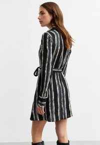 Zwart-wit gestreepte jurk met lange mouwen, een gestrikte taille en een lengte tot de knieën. Glad textuur met contrasterende lijnen en subtiele details.