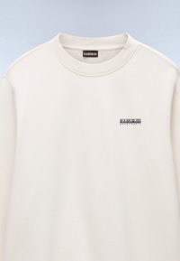 Lysebeige sweatshirt lavet af blødt stof med rund hals. Lille sort broderet logo på venstre bryst. Glat tekstur.