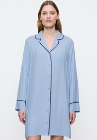 Camicia da notte azzurro chiaro realizzata in tessuto morbido, con bottone anteriore, maniche lunghe e piping nero a contrasto lungo il colletto e i polsini.
