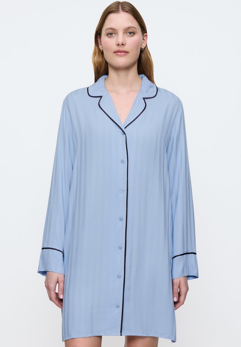 Camicia da notte azzurro chiaro realizzata in tessuto morbido, con bottone anteriore, maniche lunghe e piping nero a contrasto lungo il colletto e i polsini.