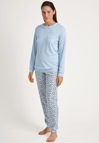 Lichtblauw shirt met lange mouwen en een borstzak, gecombineerd met witte broek met een marineblauw bloemenpatroon. Zachte stof, ontspannen pasvorm.