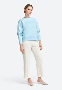 Felpa azzurro chiaro a maniche lunghe, dal taglio rilassato, abbinata a pantaloni bianchi a gamba larga e décolleté beige. Texture morbida in tutto il capo.