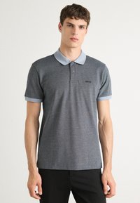 Grå kortermet polo skjorte med lyseblå krage og mansjetter, med et subtilt geometrisk mønster og svart logo på brystet.
