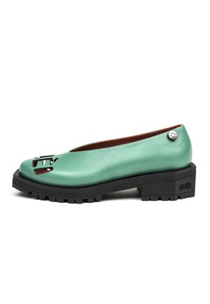 Scarpa piatta in pelle verde con suola nera spessa e scolpita, dettagli ritagliati sulla punta e piccolo bottone logo in metallo vicino al tallone.
