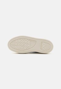 Sole béžové tenisky Converse All Star zobrazující texturovaný gumový vzor s diamantovými a liniovými designy.