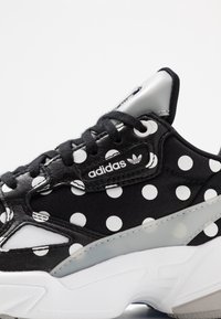 Svart sneaker med ett prickigt mönster, i läder och textilmaterial, silverdetaljer och en vit gummisula med texturerad yta.