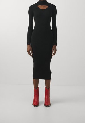 Robe midi noire à côtes avec manches longues et décolleté découpé, associée à des bottes rouges arrivant aux genoux avec des accents en clous argentés.