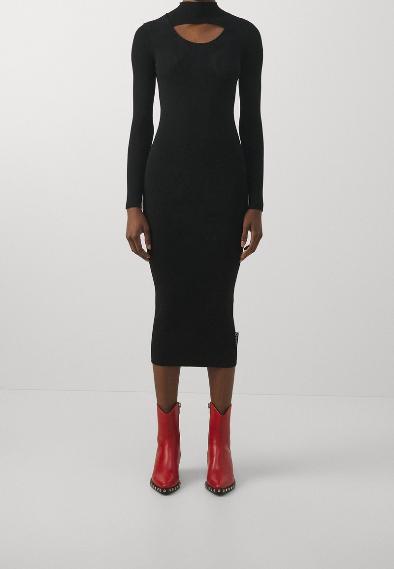 Robe midi noire à côtes avec manches longues et décolleté découpé, associée à des bottes rouges arrivant aux genoux avec des accents en clous argentés.