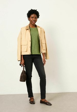 Beige cropped jacket with corduroy collar, green lightweight top, black slim jeans, brown flat shoes, and a small brown handbag.