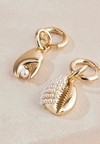 Zlato obarvani kovinski charms v obliki školjk, ena s perlom in druga okrašena z majhnimi belimi kroglicami, pritrjena na krožne zanke.
