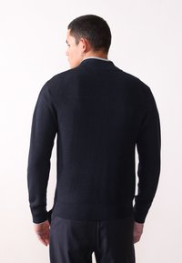 Pulover ribbed de culoare bleumarin închis, cu mâneci lungi, guler clasic și o finisare texturată. Prezintă o culoare solidă, fără modele vizibile.