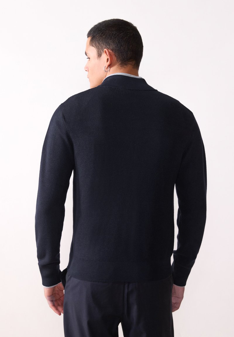 Pull-over en maille côtelée bleu marine foncé avec des manches longues, un col classique et une finition texturée. Présente une couleur unie sans motifs visibles.