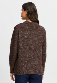 Suéter marrón de punto con un patrón texturizado, que presenta un cuello redondo y cortes laterales, exhibiendo una mezcla de colores que incluye rojo y gris.