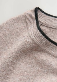 Pull-over rose clair avec un col noir côtelé. Tissu doux et texturé avec de légères variations de couleur et d'épaisseur.