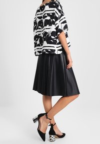 Blouse à motif noir et blanc ample, associée à une jupe plissée en cuir noir et des escarpins noirs ornés d'un talon à pois.