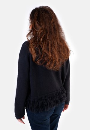 Black knit sweater with a textured fringe at the hem, featuring long sleeves and a relaxed fit, paired with dark denim jeans.