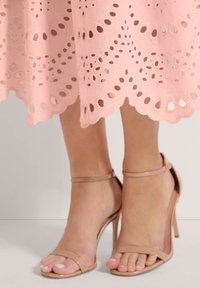 Blassrosa Spitzekleid mit Ausschnittmustern und gewelltem Saum, kombiniert mit hautfarbenen High-Heels mit dünnen Riemen und offenem Zehenbereich.