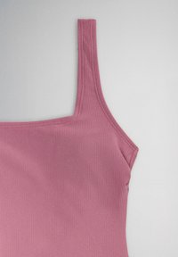 Close-up of a ribbed dusty pink tank top with a single shoulder strap on a light background.