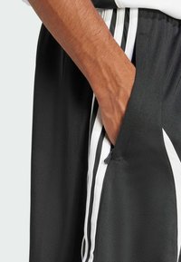 Shorts de sport noirs avec des rayures verticales blanches et des poches latérales. Fabriqués dans un matériau synthétique lisse avec une finition légèrement texturée.