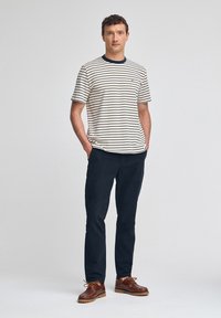 Pasiasty, krótko rękawowy t-shirt w kolorze kremowym i granatowym, zestawiony z granatowymi spodniami oraz brązowymi butami na sznurówki. Luźny krój z okrągłym dekoltem.