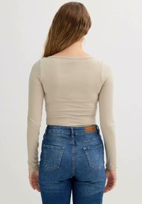 Top de manga larga acanalado beige combinado con vaqueros de tiro alto azul. Los vaqueros cuentan con dos bolsillos traseros y una etiqueta marrón en la cintura.